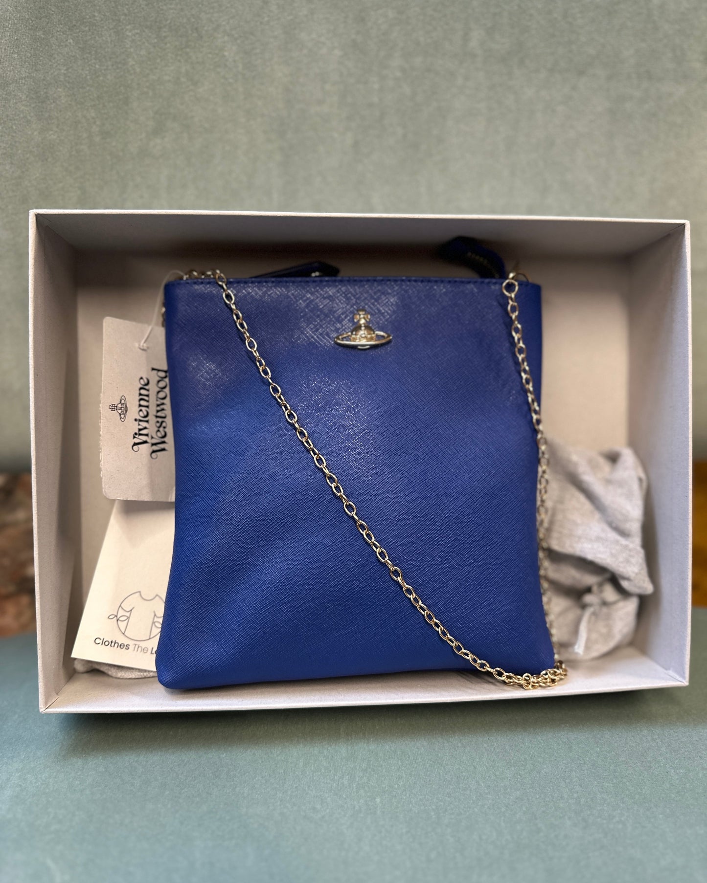 Blue handbag with a chain detail in a box on a light gray background