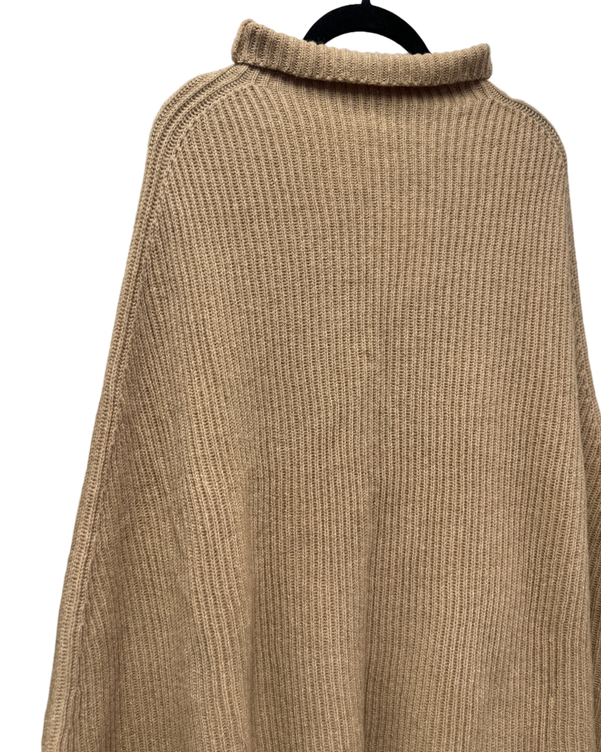 Beige ribbed sweater on a hanger against a white wall with a brick column.